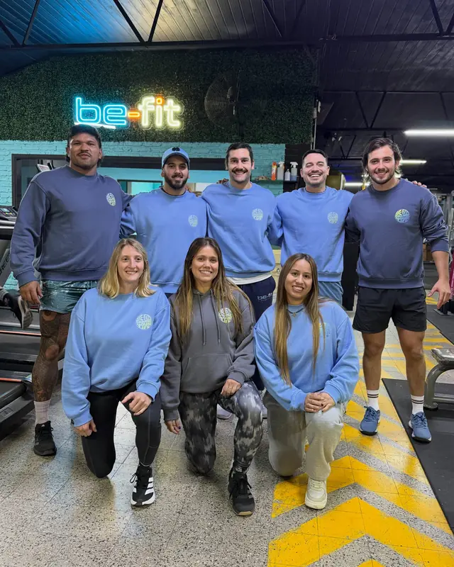 El equipo de be-fit con buzos celestes, delante del cartel en neón
