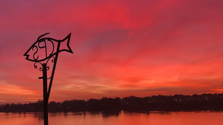Atardecer rojo sobre el río Uruguay con la escultura del pez del Club de Pesca