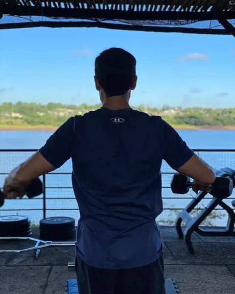 Un hombre entrena con mancuernas al aire libre, frente al río